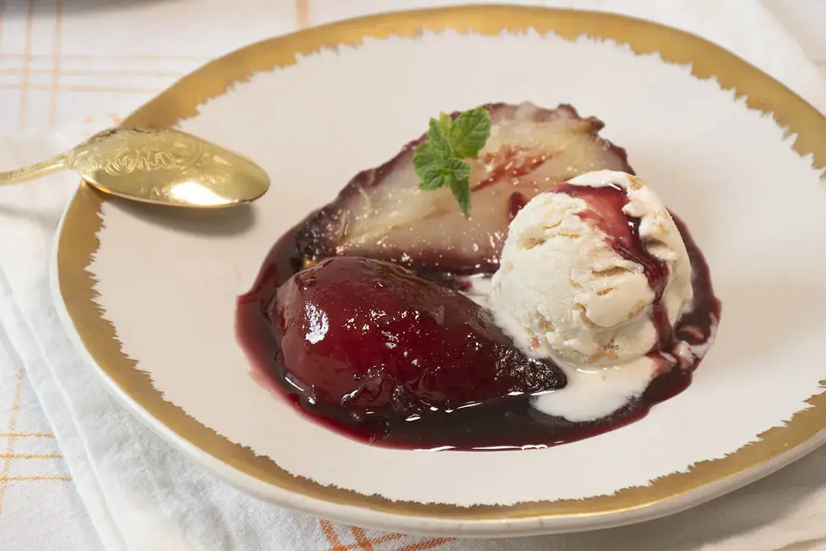 Deliciosas peras al vino tinto, servidas con una bola de helado de vainilla y una hoja de menta.