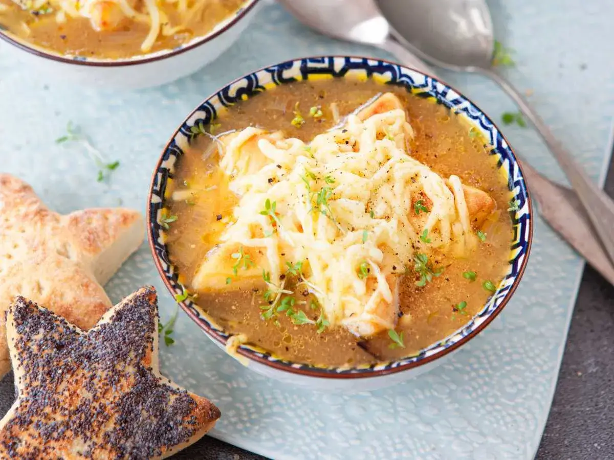 Un tazón de sopa de cebolla gratinada con queso derretido y pan con semillas de amapola en forma de estrella.