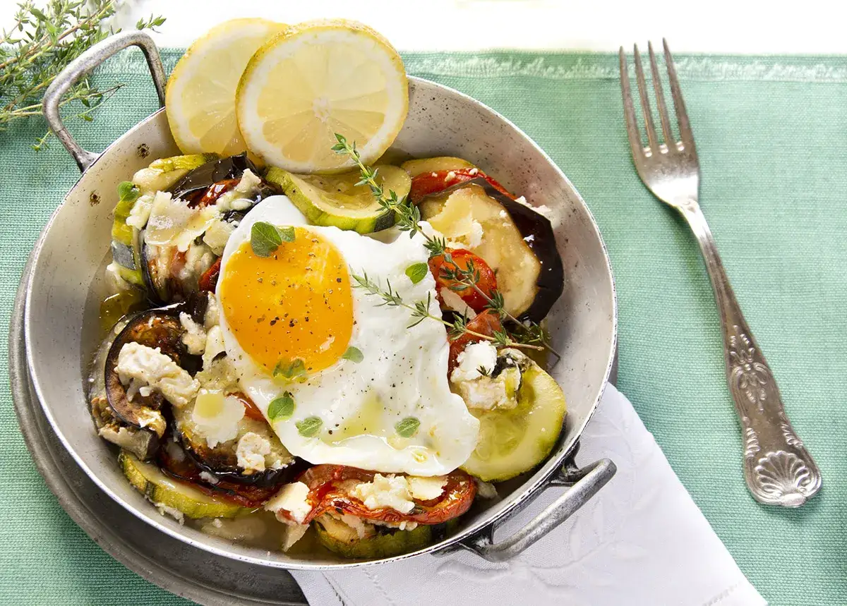Delicioso plato de verduras al horno con huevo frito, queso feta y rodajas de limón.
