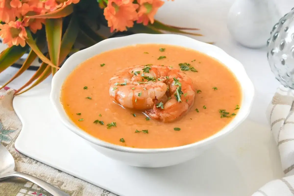 Crema de marisco servida en un cuenco blanco, decorada con un langostino y perejil picado.
