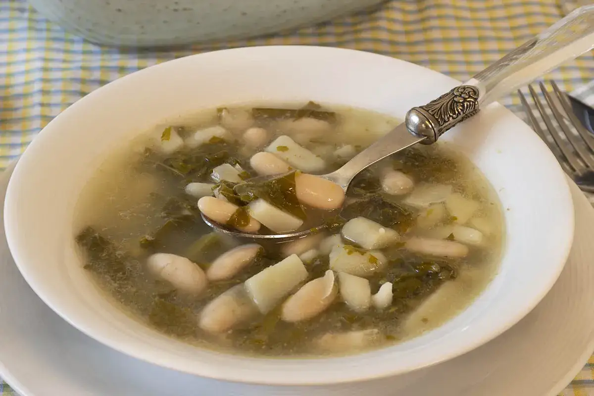 Un plato de caldo gallego con sus ingredientes: alubias blancas, patatas y grelos.