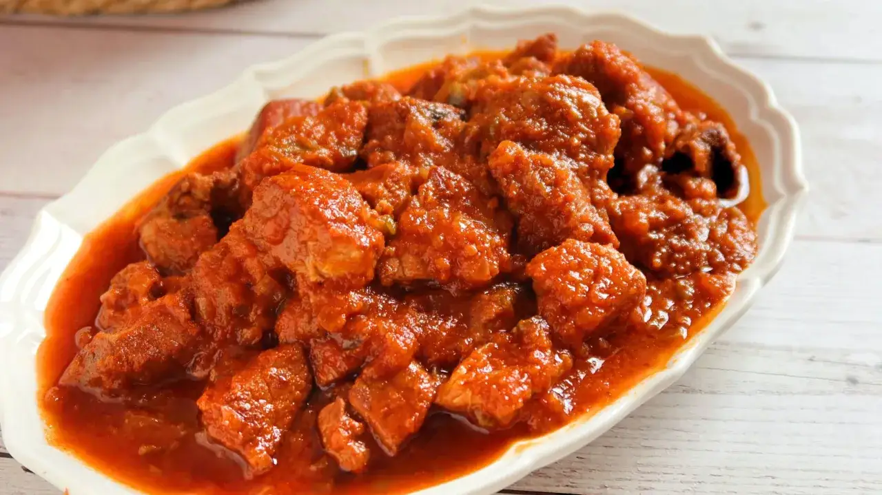 Sabroso magro con tomate, trozos de carne tierna en una rica salsa roja, servido en un plato blanco.