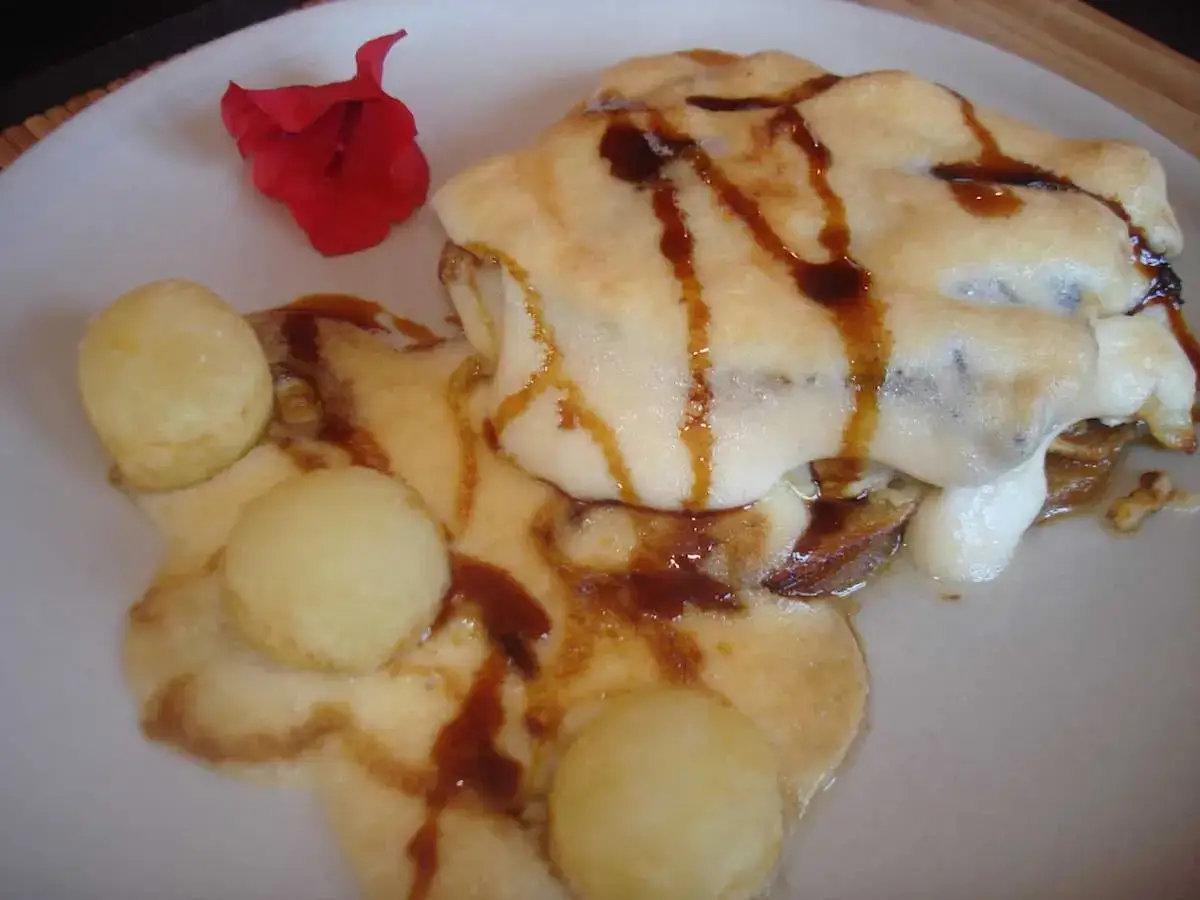 Delicioso bacalao gratinado con alioli, acompañado de pequeñas bolitas doradas y un toque de salsa oscura.