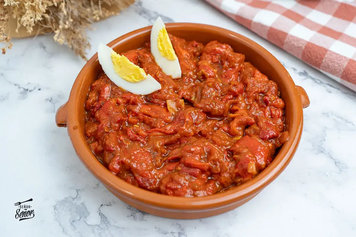 Un delicioso asadillo manchego en cazuela de barro, adornado con gajos de huevo cocido.
