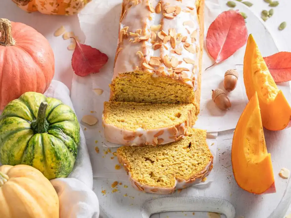 Bizcocho de calabaza, receta de la abuela, con glaseado y almendras. Rodeado de calabazas y hojas de oto&ntilde;o.