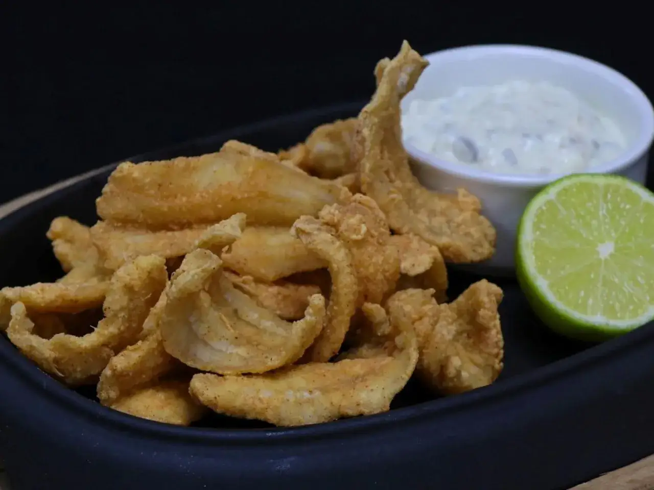 Crujiente bacaladilla frita servida con una salsa cremosa y una rodaja de lima.