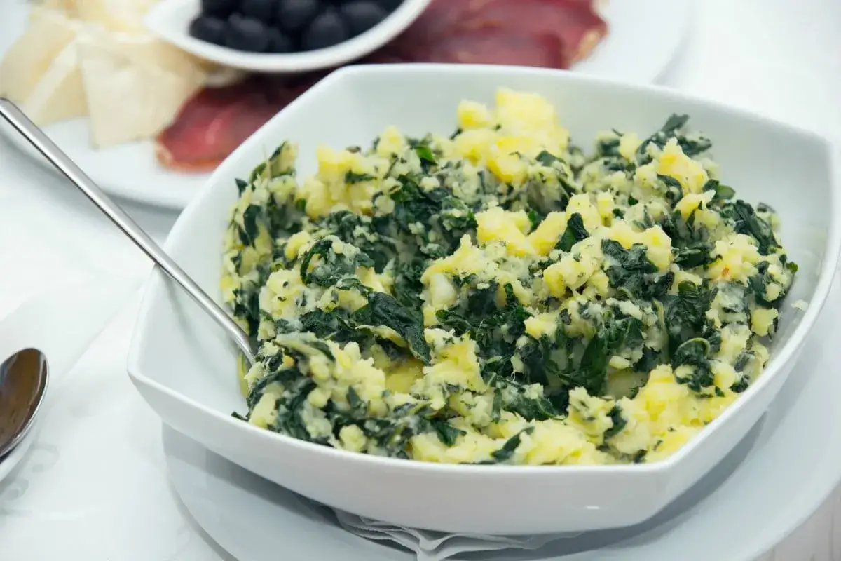 Un plato de acelgas con patatas, una mezcla rústica y sabrosa, servida en un cuenco blanco.
