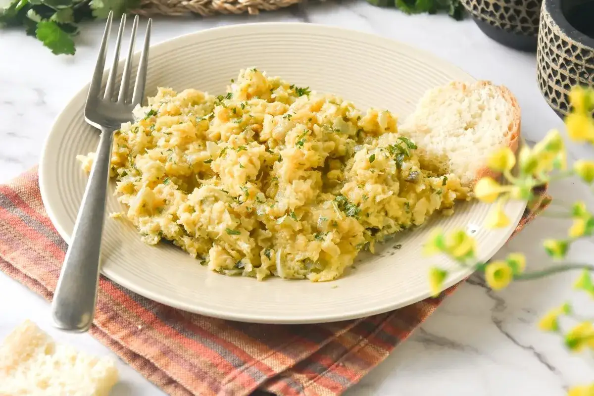Un delicioso revuelto de bacalao, esponjoso y con perejil fresco, servido con una rebanada de pan r&uacute;stico.