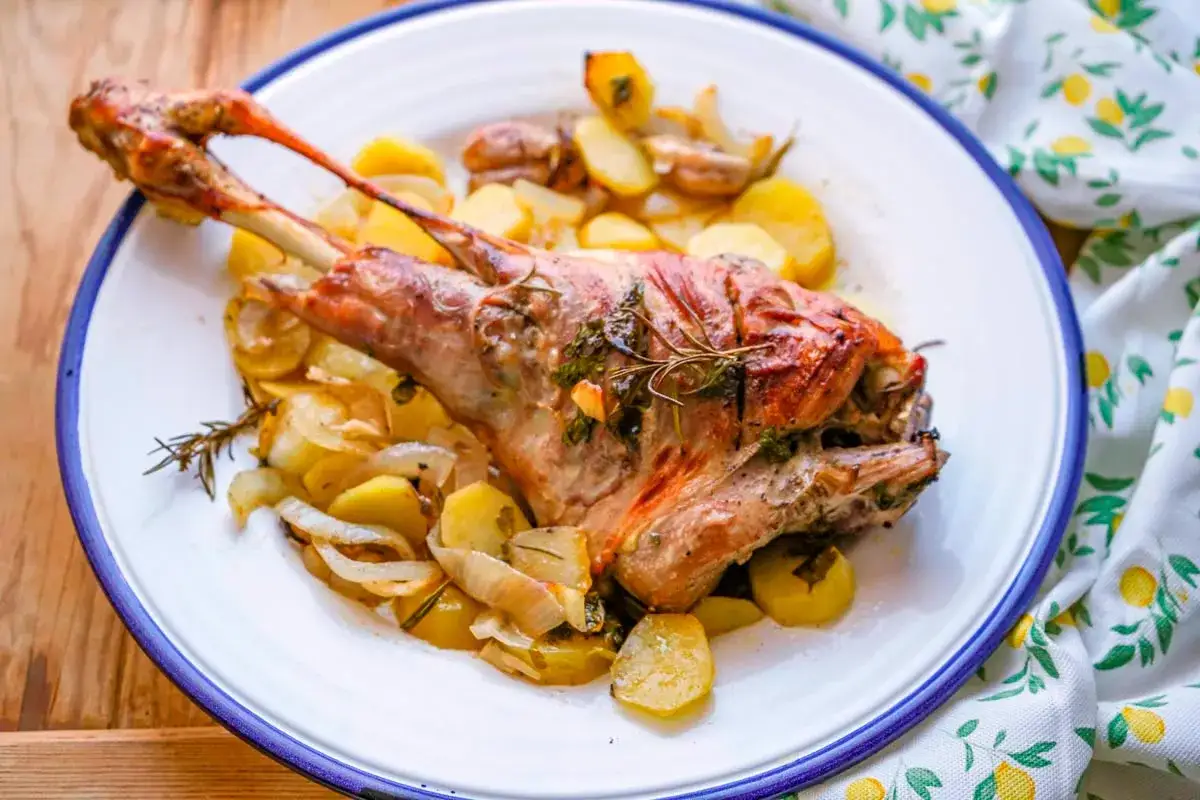 Paletilla de cordero asada con patatas y romero, un plato jugoso y aromático listo para disfrutar.