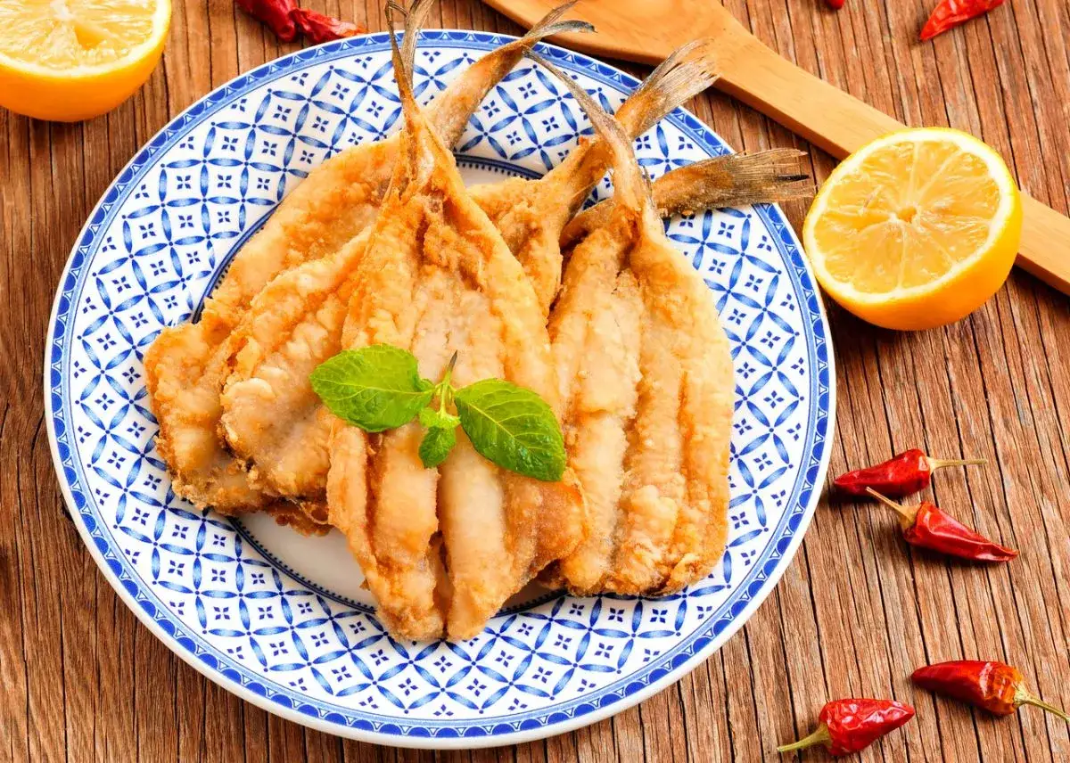 Boquerones crujientes en freidora de aire, servidos en plato azul y blanco con lim&oacute;n y guindillas.