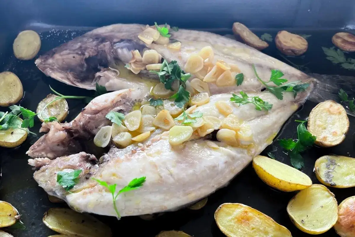 Dorada a la espalda horneada con patatas y ajo laminado, decorada con perejil fresco.