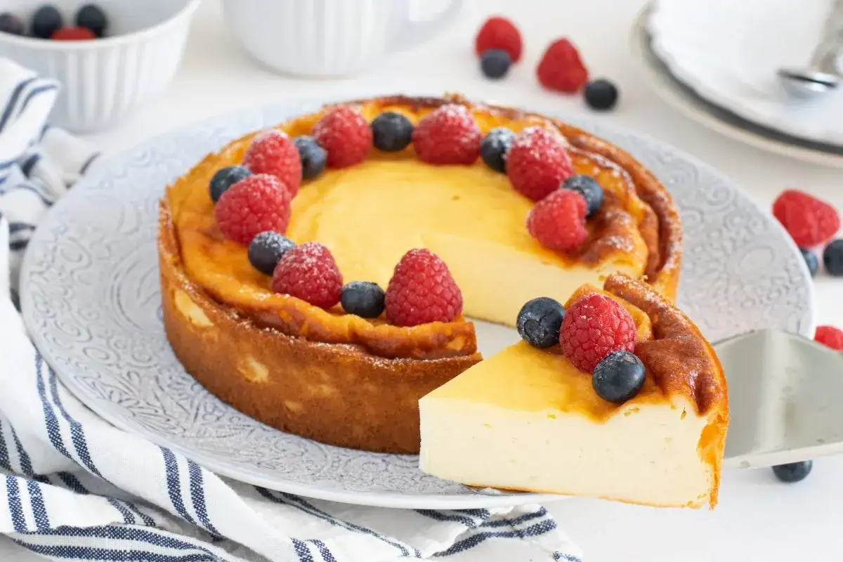 Deliciosa tarta de yogur griego, dorada y cremosa, decorada con frambuesas y arándanos frescos. ¡Un postre irresistible!