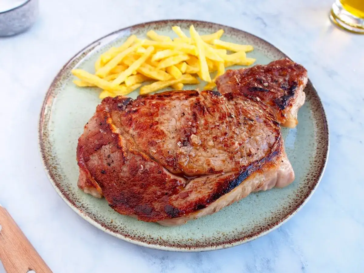 Un jugoso entrecot de ternera a la parrilla, servido con patatas fritas crujientes en un plato.