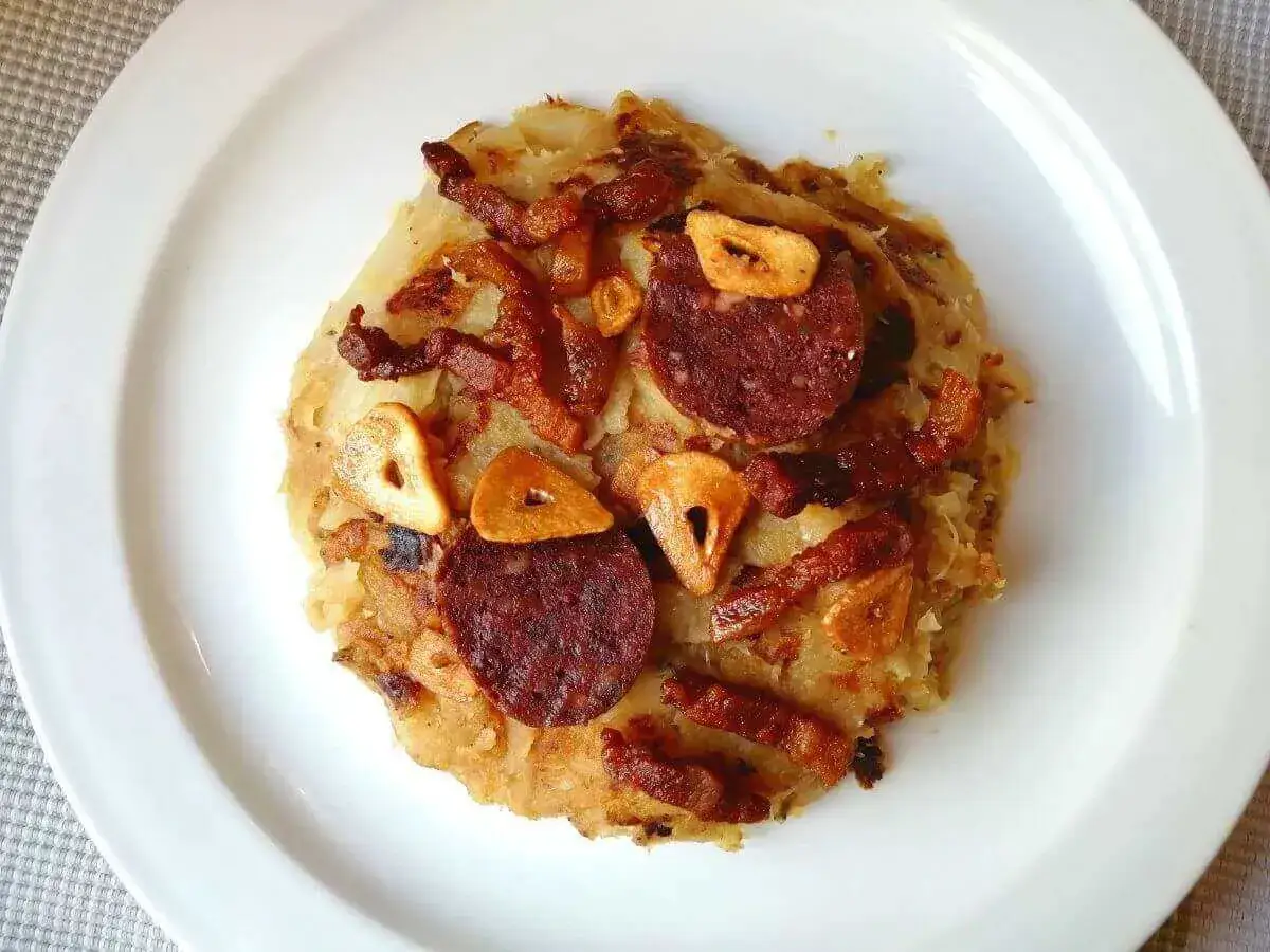 Trinxat de la Cerdanya, un plato contundente con patata, col, chorizo y ajos fritos, servido en un plato blanco.