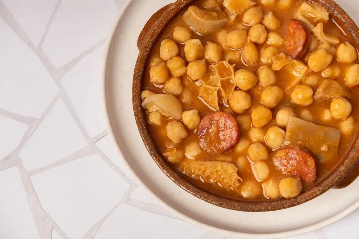 Un plato de barro con callos con garbanzos, chorizo y trozos de carne en una salsa dorada.