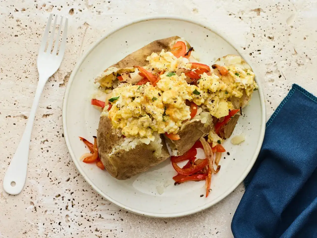 Patatas rellenas con huevo revuelto, pimientos rojos y perejil, servidas en un plato blanco.